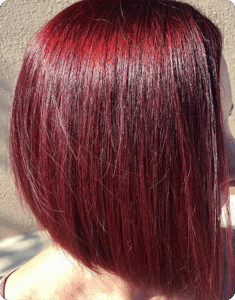 Shoulder-length straight hair dyed in a vibrant, glossy shade of deep red, shown from the side against a neutral background. | AMORE Salon, St. Petersburg, FL