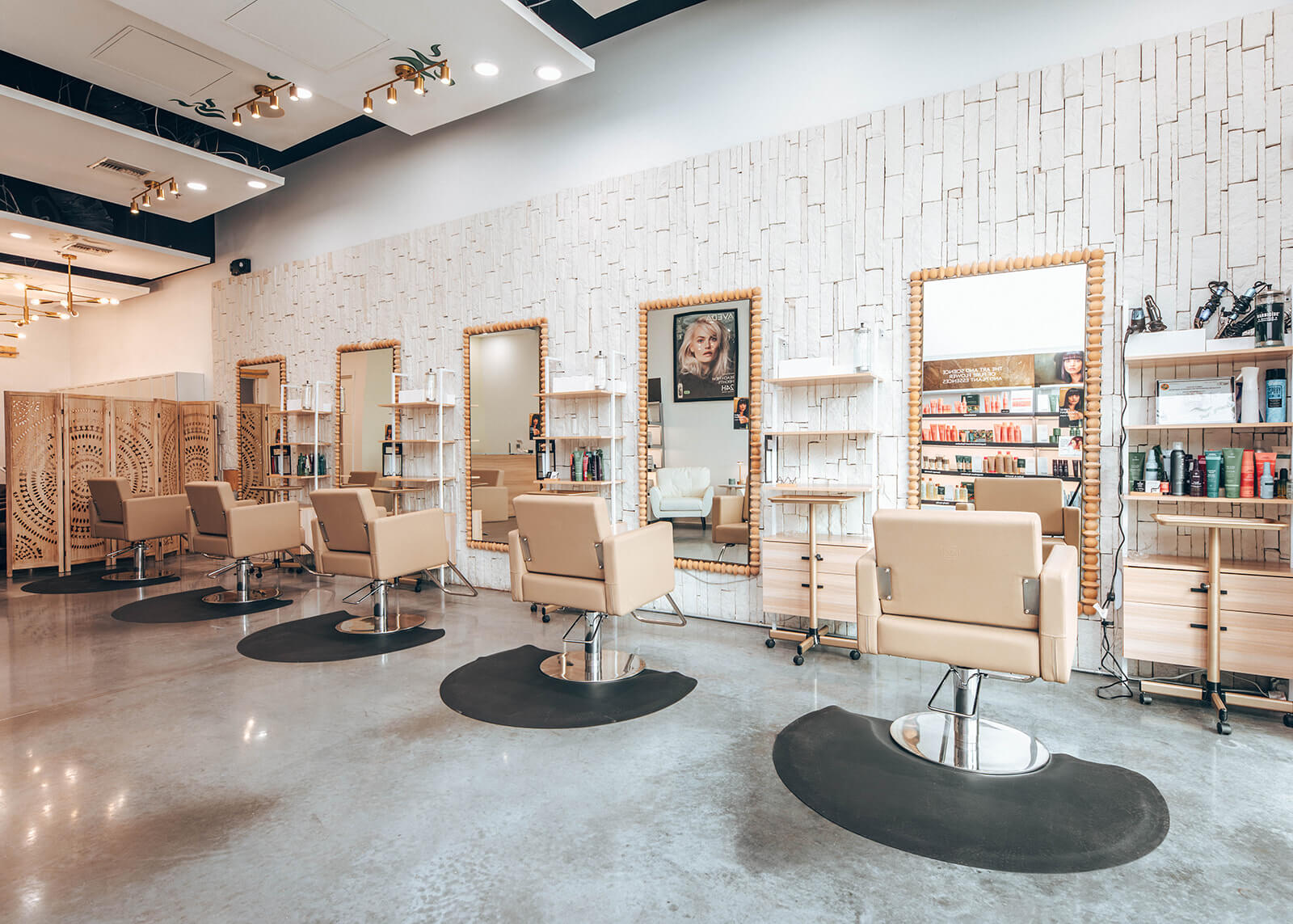 Modern hair salon interior with beige styling chairs, mirrors, shelves with hair products, and decorative wall panels on a polished concrete floor. | AMORE Salon, St. Petersburg, FL