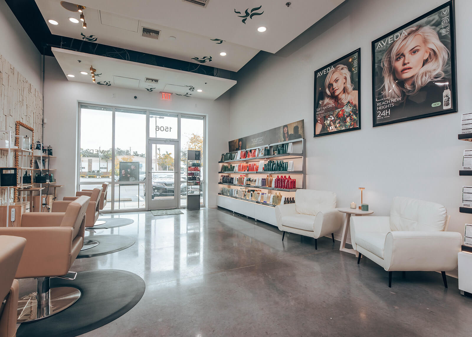 Modern hair salon interior with beige styling chairs, product shelves, two white armchairs, large windows, and posters on the wall. | AMORE Salon, St. Petersburg, FL