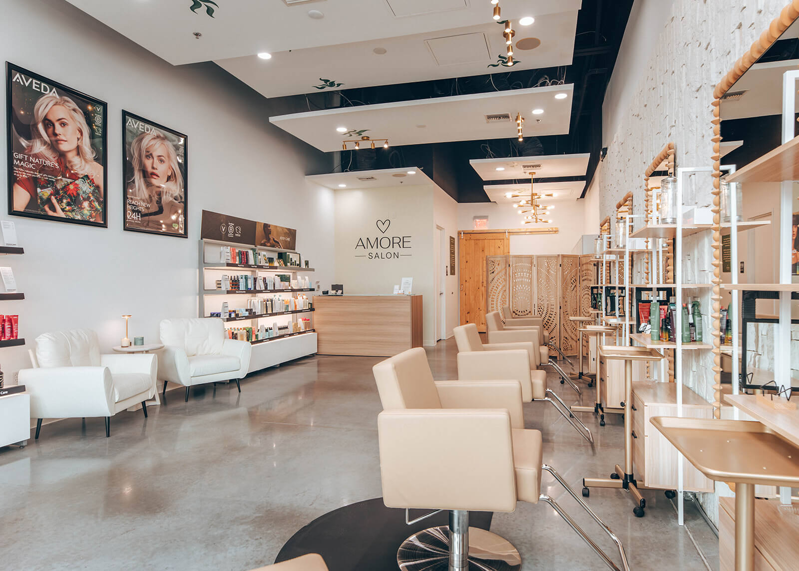 Modern hair salon interior with beige chairs, large mirrors, product displays, and a reception desk under a sign that reads “Amore Salon." The space is bright with polished floors. | AMORE Salon, St. Petersburg, FL