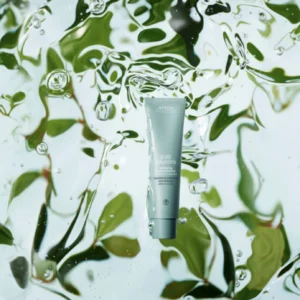 A tube of Aveda Scalp Solutions, enriched with vegan peptides, is suspended in clear water with green leaves visible in the background. | AMORE Salon, St. Petersburg, FL