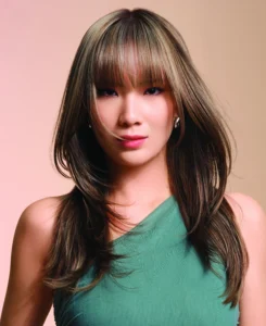 Woman with long, layered brown hair and bangs wears a green sleeveless top, facing forward against a neutral background. | AMORE Salon, St. Petersburg, FL