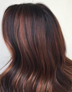 A person with long, wavy hair featuring dark brown roots and subtle reddish-brown highlights, shown from the back against a light background. | AMORE Salon, St. Petersburg, FL